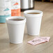 Two Dart white foam cups of coffee with sugar packets on a table.
