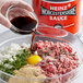 A hand pouring Heinz Worcestershire sauce into a bowl of ground meat.