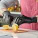 A pair of black disposable gloves being worn by a person slicing a lemon on a cutting board.