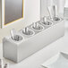 A white stainless steel flatware organizer with white cylinders holding silverware.