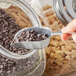 A person using a Choice aluminum scoop to scoop chocolate chips into a jar.