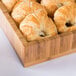 A Cal-Mil bamboo display tray filled with croissants on a hotel buffet table.