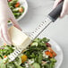 A person grating cheese on a plate of salad with a Choice stainless steel handheld grater with a black handle.