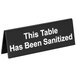 A black Tablecraft plastic sign that says "This Table Has Been Sanitized" in white and black.