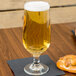 A Libbey stemmed pilsner glass of beer on a napkin next to a pretzel.