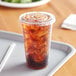 A Choice clear plastic cup filled with ice and a brown drink with a straw and flat lid.
