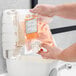 A hand pouring orange liquid from a Noble Chemical Novo Pro Series Citrus Scent hand soap refill into a sink.