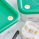 A green plastic container with a Noble Products 1" Permanent Day of the Week Clock Label on the lid.
