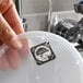 A round plastic container lid with a dissolvable day of the week clock label being rinsed under running water.