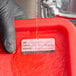A dissolvable hospital label being rinsed off a red container under running water.