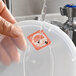 A dissolvable day of the week clock label marked for Wednesday being rinsed off a plastic container lid.