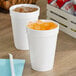 Two Dart white foam cups filled with ice and orange liquid on a table.