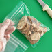 A gloved hand sealing a Clear Line plastic food bag of mushrooms.