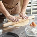 A person rolling out dough on a table with a Choice tapered French rolling pin.