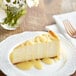 A slice of Capora White Chocolate sauce drizzled on a cheesecake with flowers on the table.