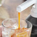A person pouring Capora Caramel Flavoring Sauce into a glass of ice and orange juice.