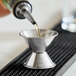 A stainless steel jigger with 0.5 oz. and 1 oz. measurement markings being used to pour liquid.