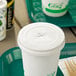 A white cup with a green EcoChoice paper lid and straw slot on a tray.