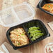 A black Choice plastic container with rice and vegetables in two compartments.