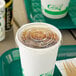 A white plastic cup with a translucent EcoChoice paper lid with a straw slot on a food court table.