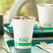 A white EcoChoice paper cold cup with green text on a tray with a white cup filled with ice tea.