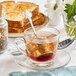 A Fox Run stainless steel tea infuser in a glass cup of tea on a saucer with toast.