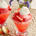 Two glasses of ice with strawberries and whipped cream on top served with spoons.