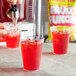 A hand pouring DominAde Fruit Punch drink mix into a glass of red liquid.