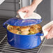 A person using a white towel to hold the lid on a Valor Galaxy Blue Enameled Cast Iron Dutch Oven filled with chicken and lemons.
