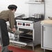 A man in a chef's hat and apron using a Vulcan 4 burner range to cook food.