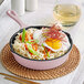A pink mini cast iron skillet with noodles, vegetables, and a fried egg on top.