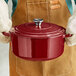 A person holding a Valor merlot enameled cast iron Dutch oven with a lid.