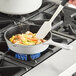 A person stirring shrimp and vegetables in a Valor Arctic White enameled cast iron skillet on a gas stove.