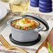 A Valor slate grey enameled mini cast iron pot with lid filled with soup, mashed potatoes, and vegetables on a table.