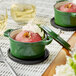 A Valor fern green enameled cast iron pot with a lid on a table with a red apple in it.