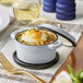 A Valor 8 oz. Glacier enameled mini cast iron pot with cover on a table of food.