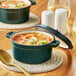 A Valor Bistro Green Enameled Mini Cast Iron Pot of soup with a lid on a coaster.