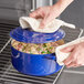 A person using a towel to hold a blue Valor enameled cast iron Dutch oven full of food.