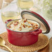 A red Valor Cranberry Apple enameled cast iron pot with food inside and a spoon on top.