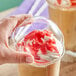 A hand holding a Choice clear plastic dome lid over a parfait with a red and white topping.