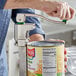 A hand using a Garde heavy-duty manual can opener to open a can of beans on a counter.