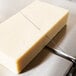 A piece of cheese being sliced with a Vollrath Redco cheese blocker on a cutting board.