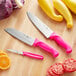 A Choice 3-piece knife set with neon pink handles on a wooden surface with a yellow squash.