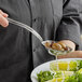 A person using a Vollrath slotted serving spoon to serve olives over a plate of lettuce.