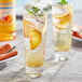 A glass of iced tea with a slice of peach and mint next to a bottle of Monin Sugar Free Peach Fruit Syrup.