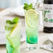 Two glasses of Monin green mint flavoring syrup with green liquid and lemon slices.