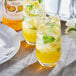 A close up of two glasses of yellow Monin mango drinks with mint leaves and ice.