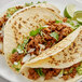 A white plate with three tacos filled with meat and vegetables.