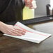 A person using a Chicopee Chix white and red foodservice towel to clean a table.