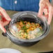 A person holding a clear container with a Visions plastic lid over a bowl of food.